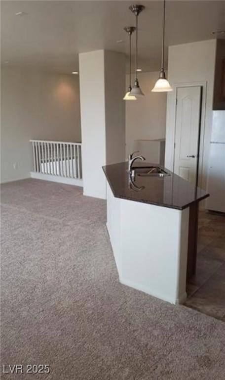 kitchen featuring an island with sink, a sink, carpet, and dark countertops