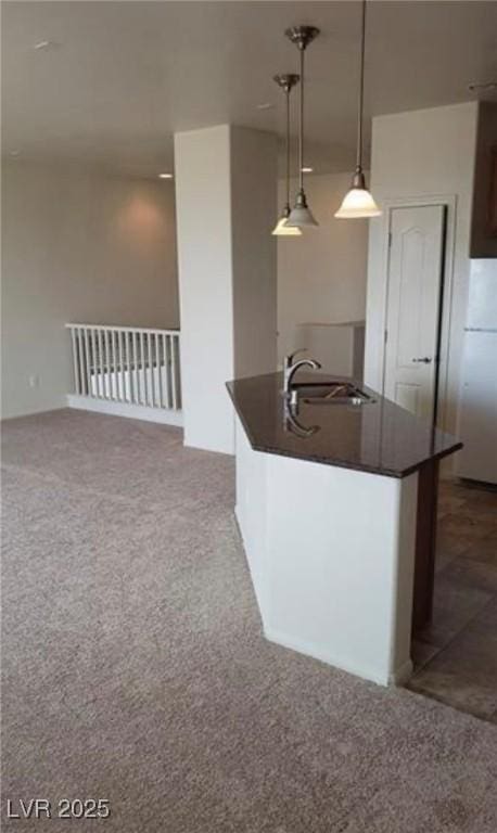 kitchen with an island with sink, dark countertops, decorative light fixtures, carpet, and a sink