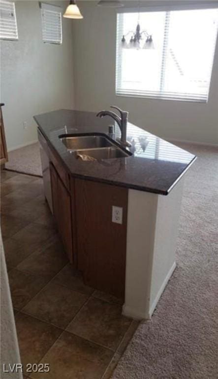 kitchen featuring tile patterned floors, dark countertops, a kitchen island with sink, white dishwasher, and a sink