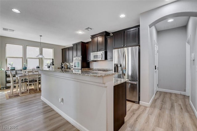 11036 Mount Hunter St, Las Vegas, NV 89179 - kitchen featuring stainless steel appliances, arched walkways, light wood-style floors, a center island with sink, and dark brown cabinetry