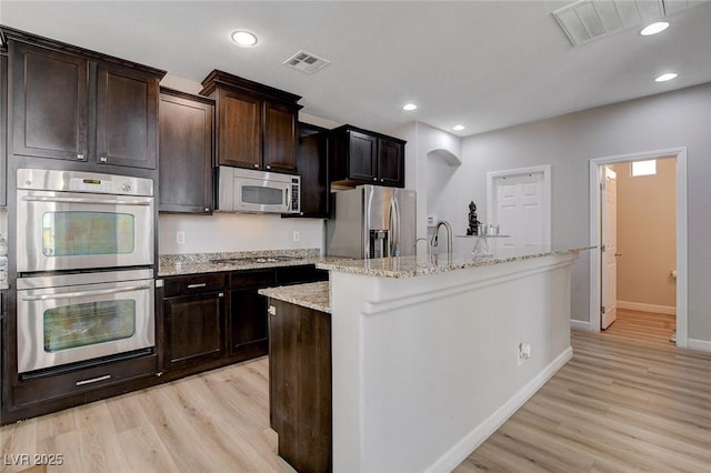 kitchen featuring appliances with stainless steel finishes, a kitchen island with sink, light wood-style floors, baseboards, and recessed lighting