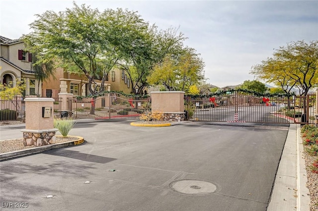 view of asphalt road featuring a gate, a gated entry, and curbs