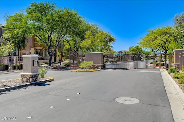 view of asphalt street with curbs, a gated entry, and a gate