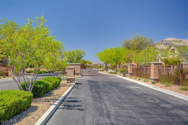 view of asphalt street with curbs, a gated entry, a gate, and a residential view