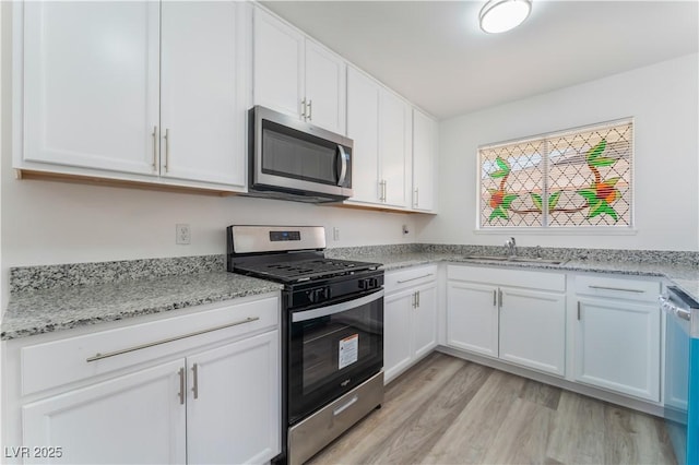 kitchen with a sink, appliances with stainless steel finishes, light stone counters, and white cabinetry