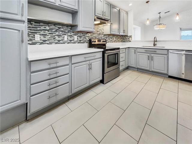 kitchen with gray cabinetry, under cabinet range hood, decorative backsplash, stainless steel appliances, and a sink