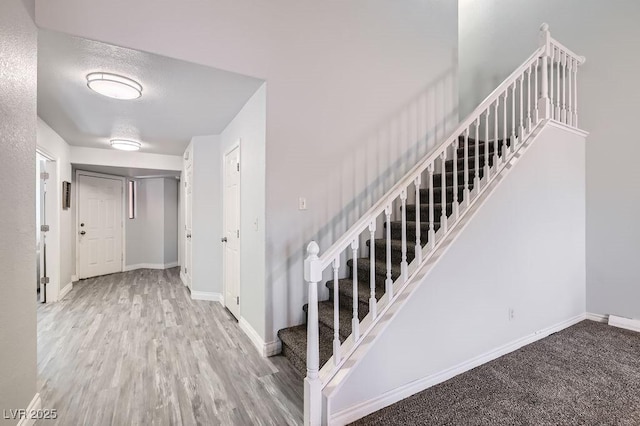 staircase with baseboards, wood finished floors, and a textured ceiling
