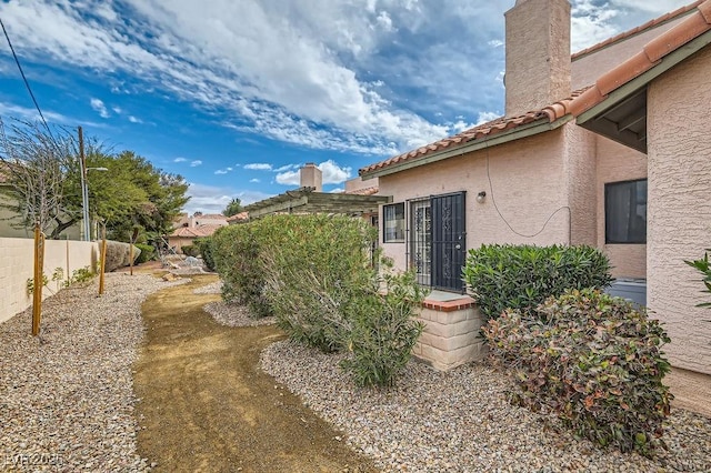 view of home's exterior featuring a tiled roof, fence, stucco siding, and a chimney