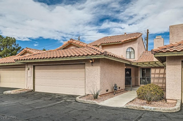 mediterranean / spanish house featuring an attached garage, aphalt driveway, stucco siding, and a tile roof