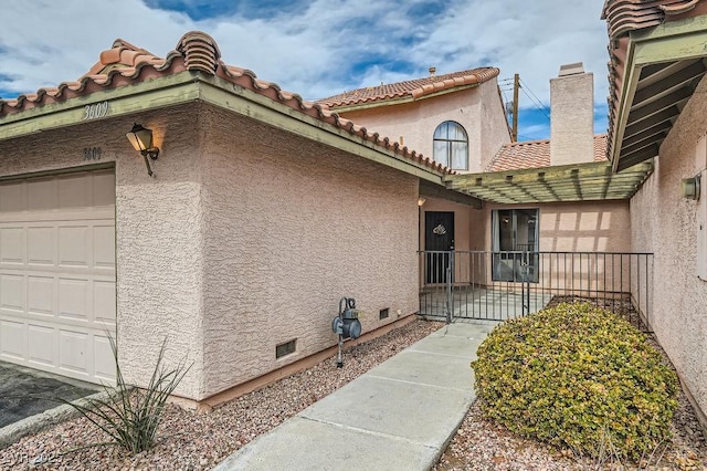 entrance to property with an attached garage, a tiled roof, stucco siding, and crawl space