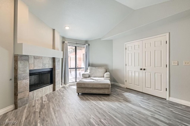 sitting room with a tiled fireplace, baseboards, wood finished floors, and vaulted ceiling