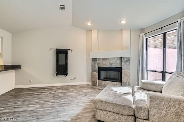 living room with visible vents, baseboards, a fireplace, vaulted ceiling, and wood finished floors