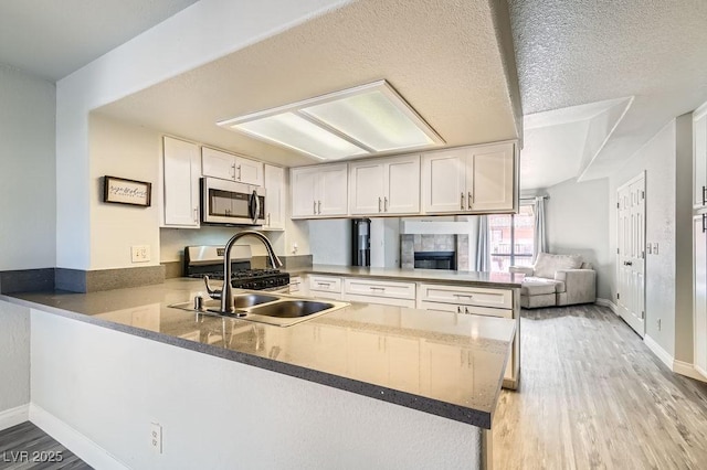 kitchen with a peninsula, a textured ceiling, white cabinetry, stainless steel appliances, and light wood-style flooring