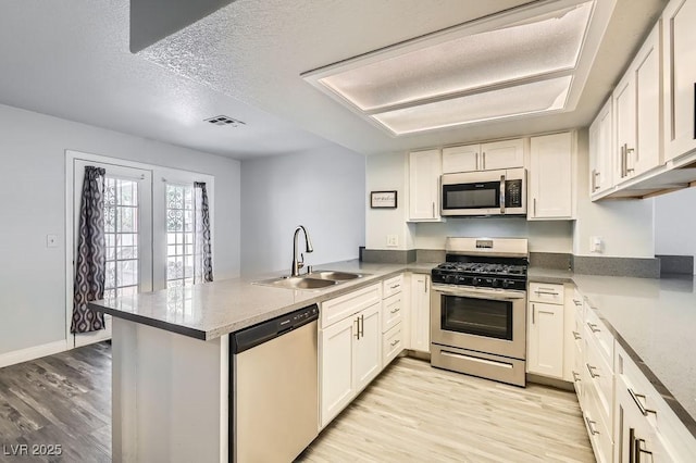 kitchen with stainless steel appliances, a peninsula, light wood-style flooring, and a sink