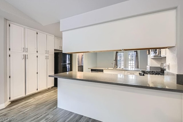 kitchen with a peninsula, light wood-style flooring, white cabinets, appliances with stainless steel finishes, and a sink