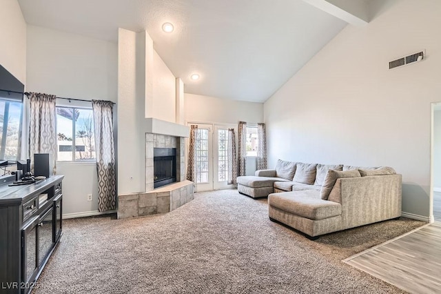 living area featuring baseboards, carpet floors, visible vents, high vaulted ceiling, and a tile fireplace