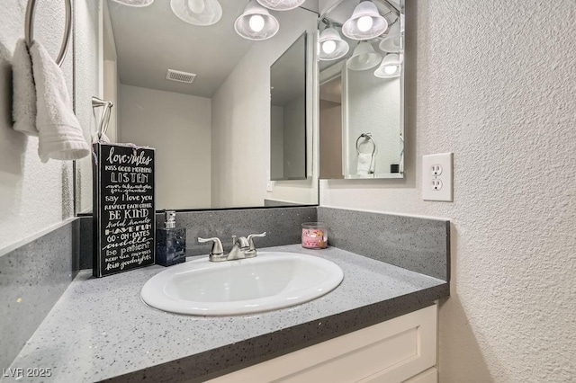 bathroom featuring a textured wall, vanity, and visible vents
