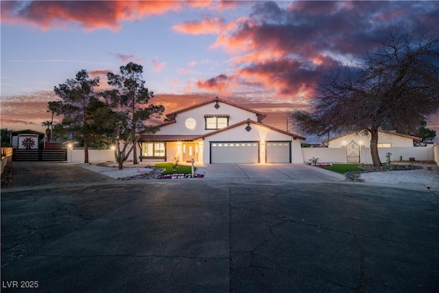mediterranean / spanish-style house featuring an attached garage, fence, stucco siding, a gate, and driveway