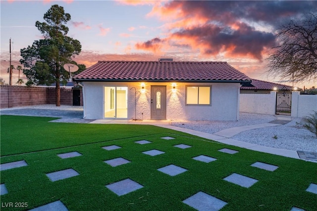 back of house at dusk featuring a tile roof, a gate, fence private yard, and stucco siding