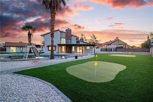 back of property at dusk featuring a patio area, fence, stucco siding, an outdoor pool, and a balcony