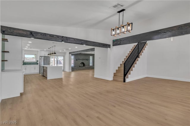 unfurnished living room featuring baseboards, stairs, visible vents, a brick fireplace, and light wood finished floors