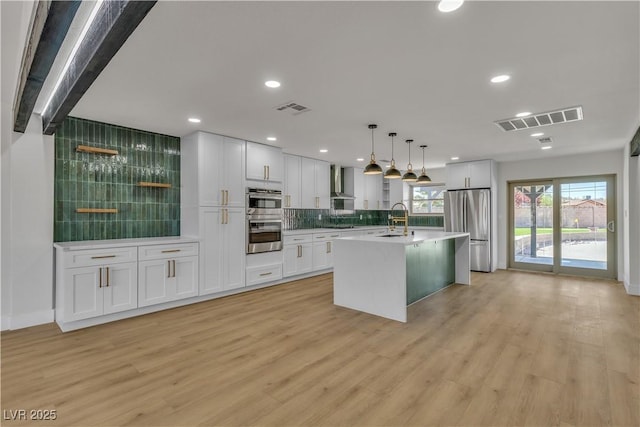 kitchen with visible vents, a sink, wall chimney range hood, light wood finished floors, and stainless steel appliances