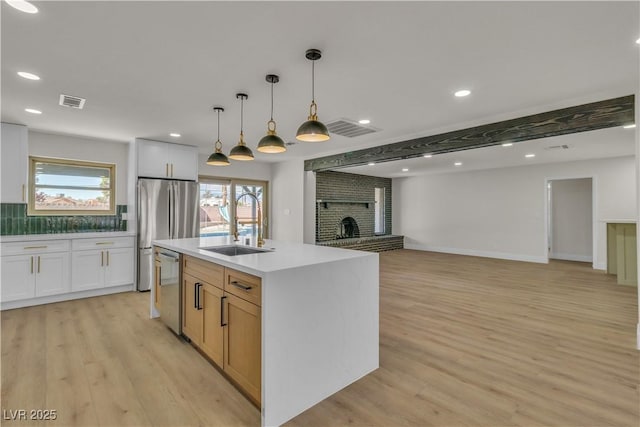 kitchen with a fireplace, light wood-type flooring, a sink, and appliances with stainless steel finishes