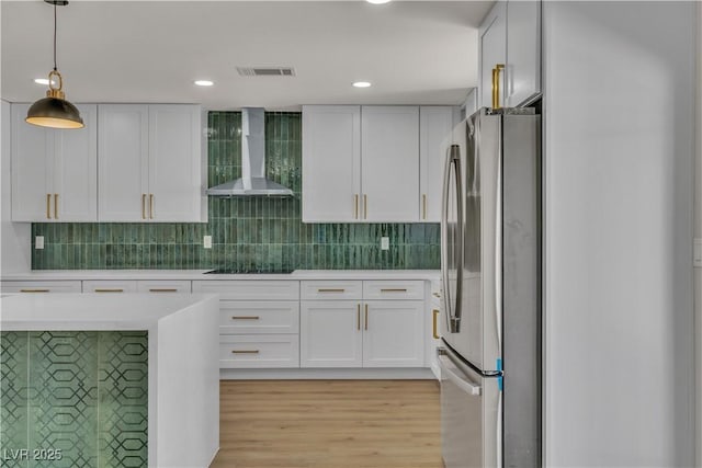 kitchen featuring visible vents, wall chimney exhaust hood, light countertops, freestanding refrigerator, and black electric stovetop