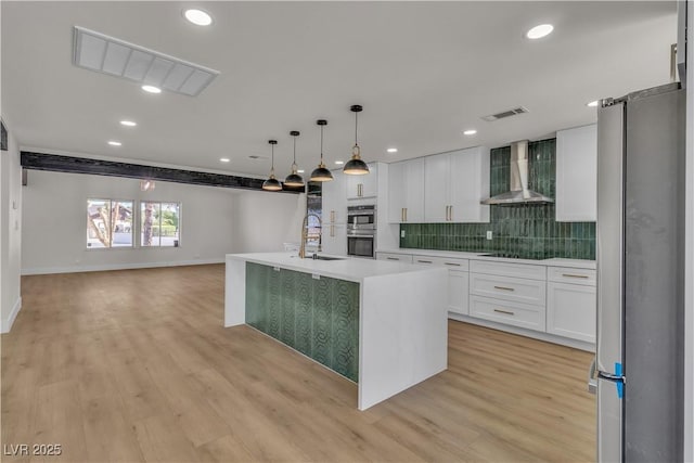 kitchen featuring light wood-style floors, visible vents, wall chimney exhaust hood, stainless steel appliances, and a sink