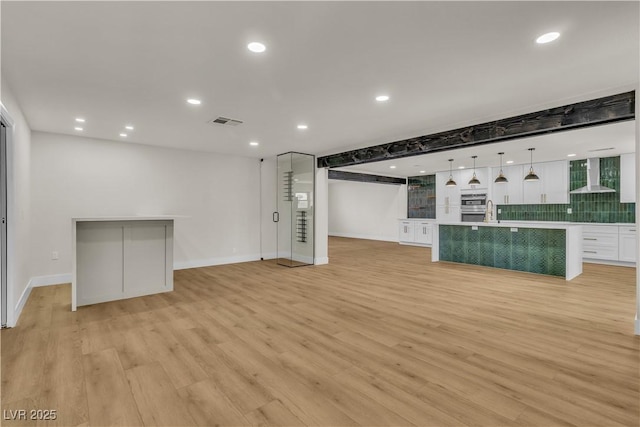 interior space featuring wall chimney range hood, open floor plan, white cabinetry, visible vents, and light wood finished floors