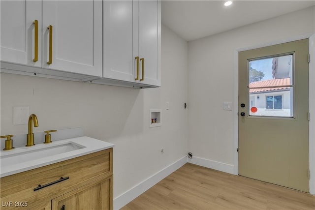 clothes washing area featuring baseboards, washer hookup, light wood-style floors, cabinet space, and a sink