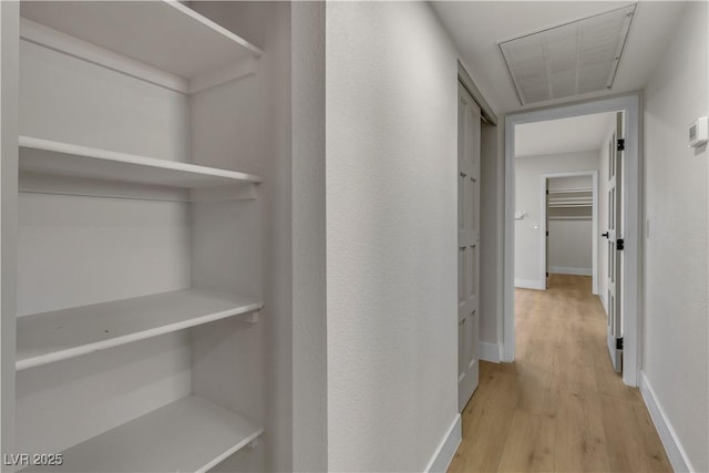 corridor with light wood-style flooring, attic access, and baseboards