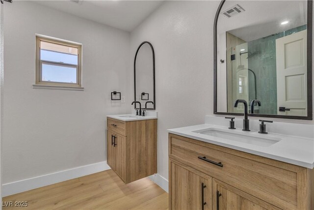 full bath with two vanities, a shower stall, visible vents, a sink, and wood finished floors