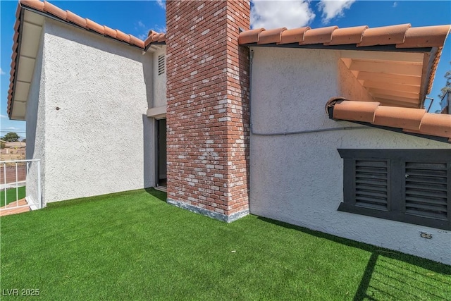 view of side of property with a yard, a tiled roof, stucco siding, and a chimney