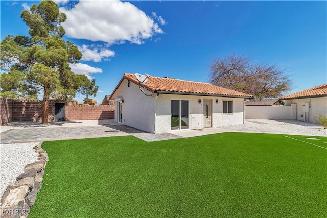 rear view of house with a tiled roof, a yard, a fenced backyard, stucco siding, and a patio area