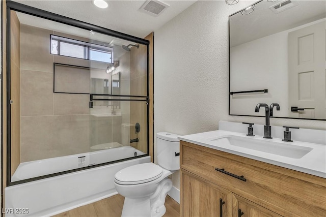 bathroom featuring bath / shower combo with glass door, vanity, visible vents, and toilet
