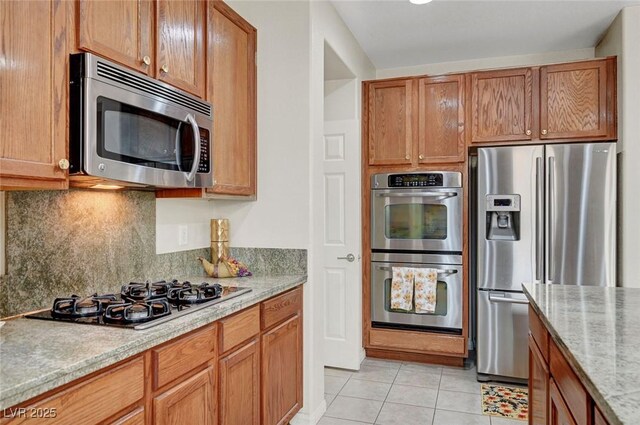 7216 Campolina Ct, Las Vegas, NV 89113 - kitchen featuring light stone counters, decorative backsplash, brown cabinets, light tile patterned floors, and appliances with stainless steel finishes