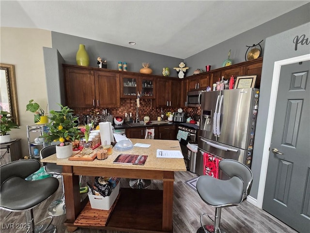 kitchen featuring glass insert cabinets, a peninsula, wood finished floors, stainless steel appliances, and backsplash
