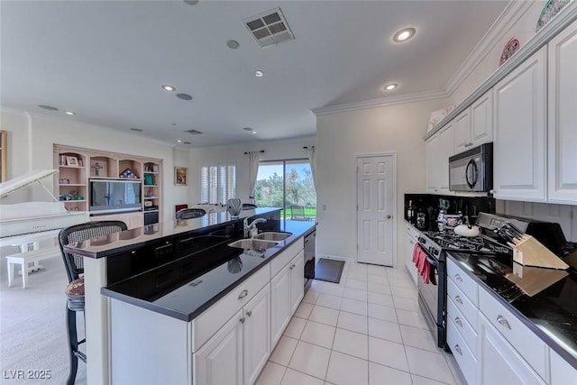 kitchen featuring visible vents, a sink, black microwave, range with gas stovetop, and a breakfast bar area