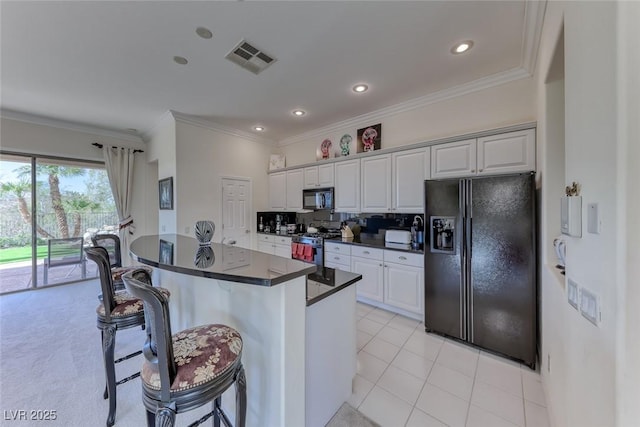 kitchen featuring visible vents, dark countertops, a kitchen breakfast bar, crown molding, and black appliances