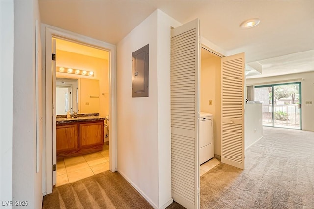 corridor with baseboards, electric panel, light tile patterned floors, washer / dryer, and light colored carpet