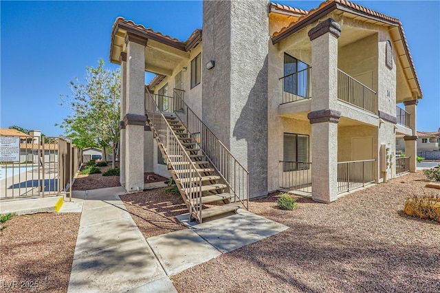 view of side of home featuring fence, a tile roof, stairway, and stucco siding