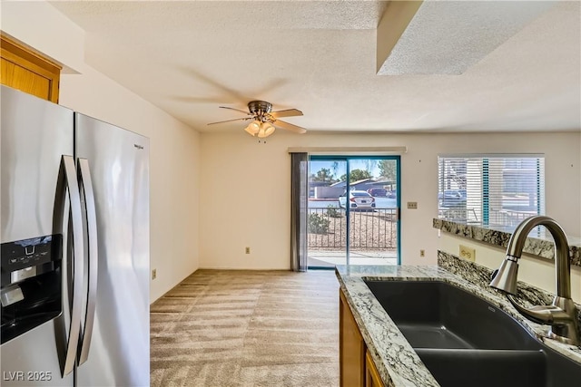 kitchen with stainless steel fridge with ice dispenser, brown cabinetry, light colored carpet, a ceiling fan, and a sink