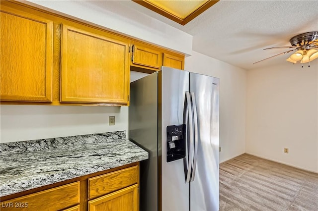 kitchen featuring stainless steel fridge, light countertops, a ceiling fan, brown cabinetry, and light carpet