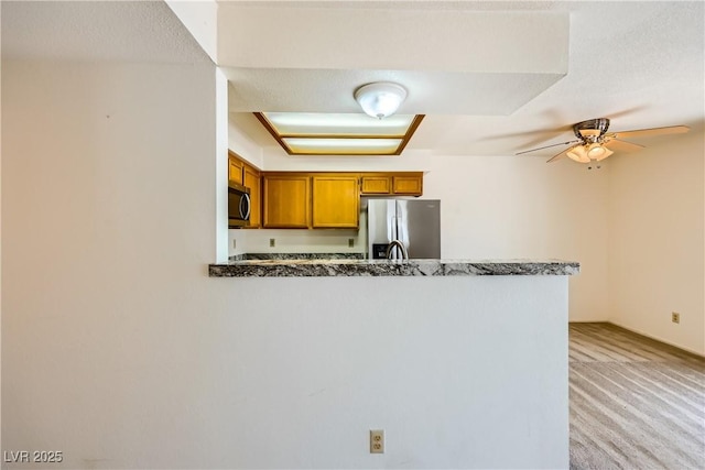 kitchen with light carpet, a peninsula, a ceiling fan, brown cabinets, and appliances with stainless steel finishes
