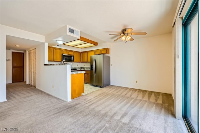 kitchen with ceiling fan, brown cabinetry, a peninsula, light colored carpet, and stainless steel appliances