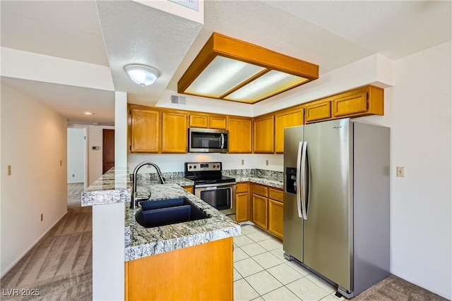 kitchen featuring a peninsula, a sink, visible vents, brown cabinetry, and appliances with stainless steel finishes