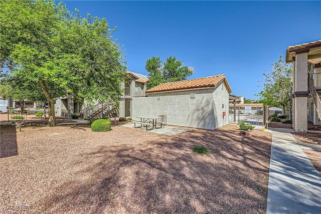 rear view of house with a tile roof, stairway, stucco siding, a residential view, and a gate