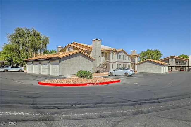 view of front of property featuring a chimney, stucco siding, community garages, and a tiled roof