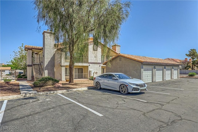 view of front facade with community garages, stucco siding, uncovered parking, a chimney, and a tile roof